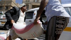 People carry a sack of wheat to a van outside a food distribution center for poor families in Yemen capital Sanaa